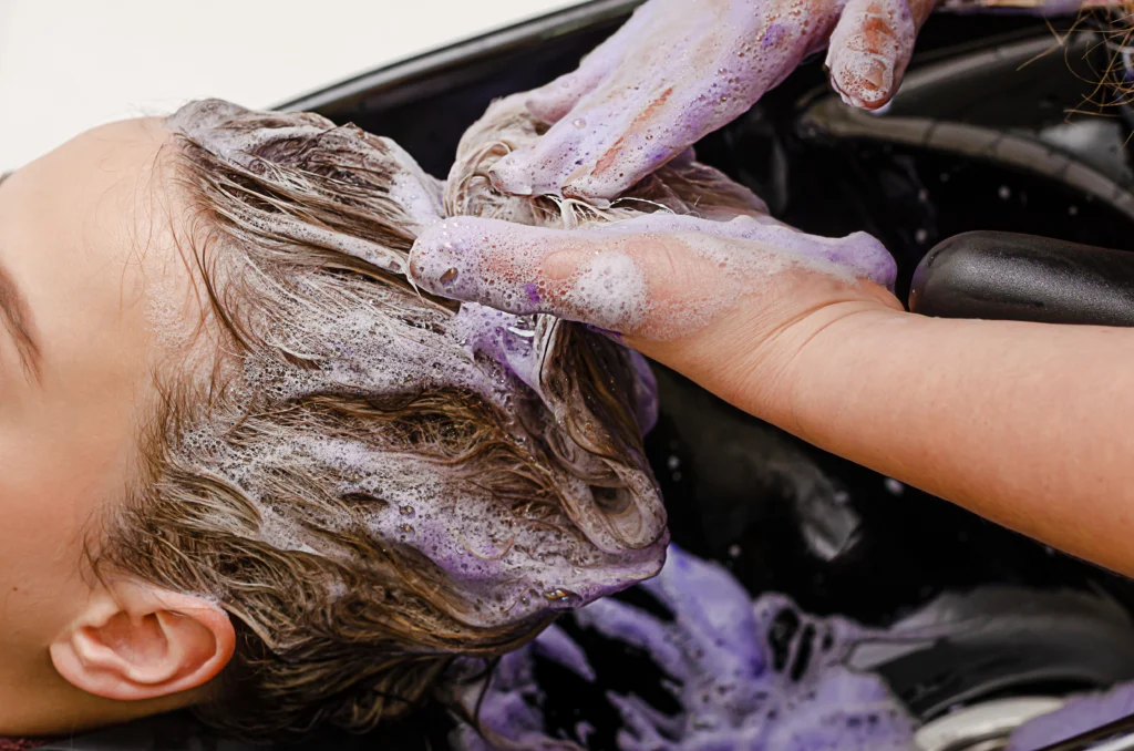 close up of stylist applying purple shampoo to hair in a salon