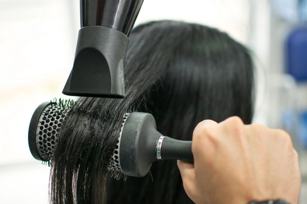 close up of hair being brushed on a round brush while being blow dried in a hair salon